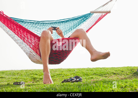 Kaukasischen Mann zum Entspannen in der Hängematte mit Handy Stockfoto