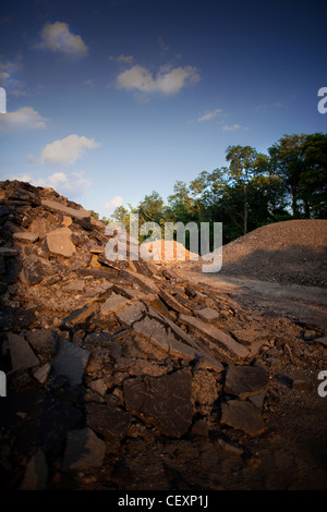 Baustelle. Einfache, saubere vertikale Farbfoto. Haufenweise Kies, Asphalt, mit Bäumen im Hintergrund, blauer Himmel gebrochen. Stockfoto
