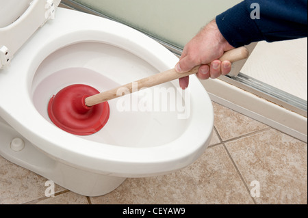 Ein Klempner verwendet einen Kolben um eine Toilette zu reinigen. Stockfoto