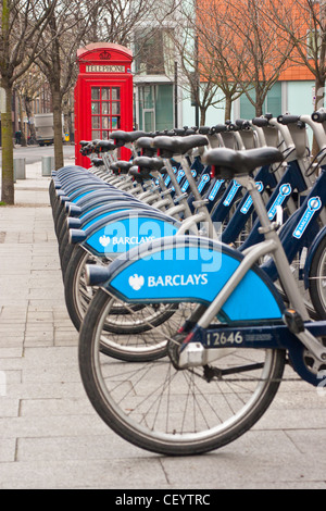 Eine Reihe von Fahrrädern für Londons Cycle Hire Schema vor eine rote Telefonzelle an einem Messestand mieten in Southwark aufgereiht. Stockfoto