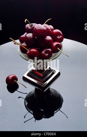 Rote Kirschen häuften sich in einem silbernen Kristallschale in eine verspiegelte Oberfläche reflektiert Stockfoto