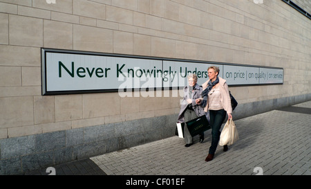 Weibliche Käufer mit Tragetaschen vorbei gehen die John Lewis store Slogan nie bewusst unterboten in Cardiff Wales UK KATHY DEWITT Stockfoto