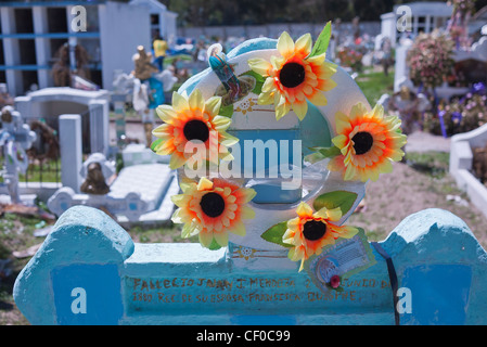 Ein Kranz aus künstlichen Blumen hängt an einem Kreuz geformten Grabstein auf einem Friedhof auf dem Quilotoa Loop in Ecuador. Stockfoto