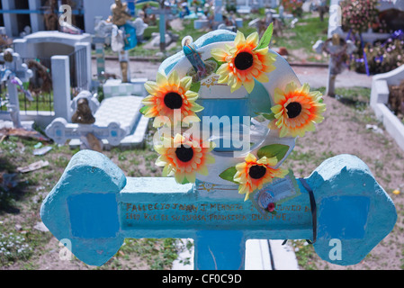 Ein Kranz aus künstlichen Blumen hängt an einem Kreuz geformten Grabstein auf einem Friedhof auf dem Quilotoa Loop in Ecuador. Stockfoto