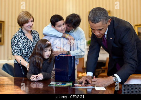 Präsident Barack Obama unterzeichnet Elemente für Make-A-Wish Kind Rafael Mullet während eines Besuchs im Oval Office 25. Januar 2012 in Washington, DC. . Rafael wird von seiner Mutter Maria Velez, Rafael Mullet Vater und Schwester Maria Mullet begleitet. Stockfoto