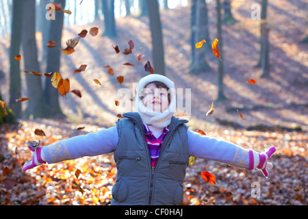 Schöne 7-jährige Mädchen wirft Blätter im Wald. Stockfoto