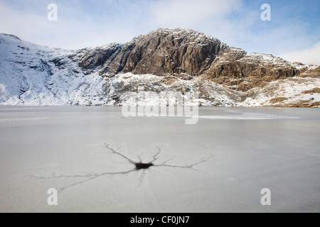 Eine gefrorene scheut Tarn mit Riss Muster in das Eis über dem Langdale Tal im Lake District, Großbritannien mit Pavey Arche Stockfoto