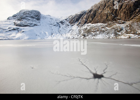 Eine gefrorene scheut Tarn mit Riss Muster in das Eis über dem Langdale Tal im Lake District, Großbritannien mit Pavey Arche Stockfoto