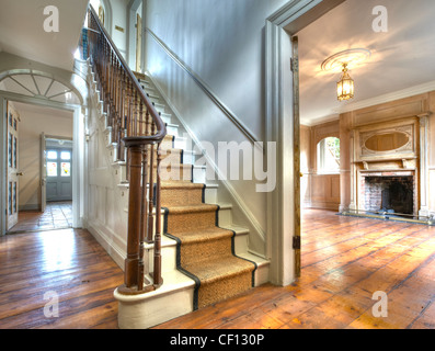 Ein Weitwinkel Schuss eines alten, aber renovierten Haus innen zeigt ein zentrales Treppenhaus zwei Empfangsräume mit Holzboden. Stockfoto