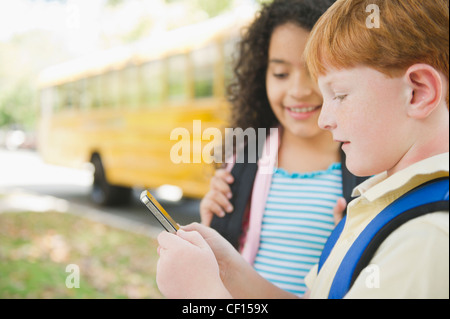 Kinder mit Handy während des Wartens auf Schulbus Stockfoto