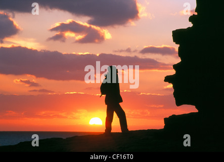 Eine einsame Gestalt steht thront auf oben auf einer Klippe am Nash Punkt Silhoutted bei Sonnenuntergang. Stockfoto