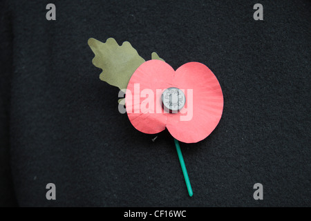 Eine englische künstliche Royal British Legion rote Mohn auf eine dunkle Jacke Hintergrund.  Dies zeigt das grüne Blatt nach oben. (11:00) Stockfoto