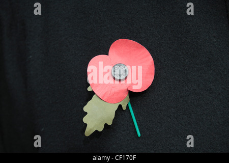 Eine englische künstliche Royal British Legion rote Mohn auf eine dunkle Jacke Hintergrund.  Dies zeigt das grüne Blatt nach unten. (06:00) Stockfoto