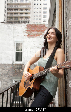 Frau spielt Gitarre auf Feuerleiter Stockfoto