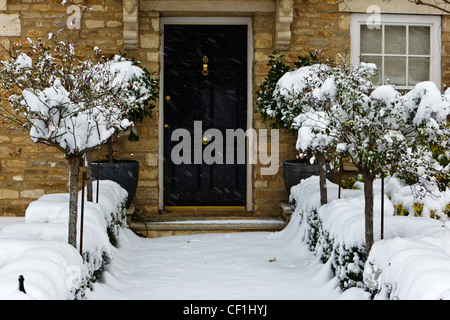 Einen schneebedeckten Weg bis zu erbaute eine schwarzen Haustür von einem Stein Haus in den Cotswolds. Stockfoto