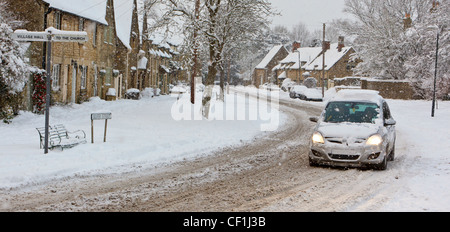 Ein Auto durch fallende Schnee kämpfen auf Silver Street in Cotswolds Dorf von South Cerney. Stockfoto