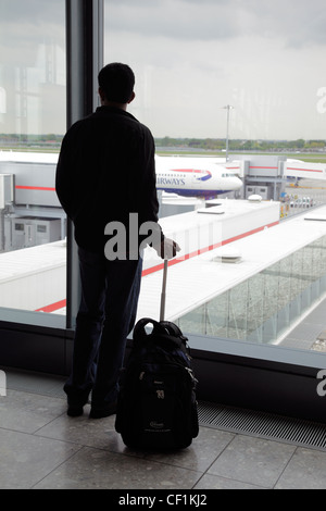 Silhouette eines Passagiers stehend mit seiner Reisetasche Blick aus einem Fenster in der Abflughalle des Flughafens Heathrow. Stockfoto