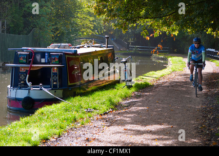 Ein Radfahrer Reiten entlang der Leinpfad vorbei an einem Hausboot am Oxford-Kanal im Herbst. Stockfoto