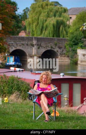 Eine Frau sitzt auf einem Stuhl am Ufer der Themse Sonntagszeitung lesen. Stockfoto