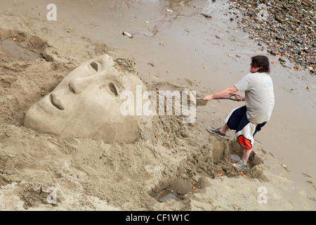 Ein Künstler Bildhauerei einen Kopf im Sand am Ufer in der Nähe von Waterloo in London South Bank. Stockfoto