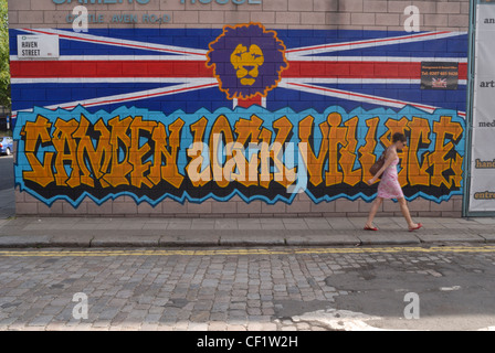 Eine Frau, die ein Gemälde an der Wand im Haven Street, Camden, mit dem Kopf eines Löwen über die Worte Camden Lock Vill vorbeigehen Stockfoto