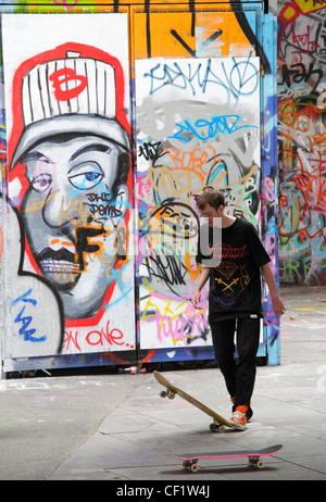 Ein Skateboarder vor dem Hintergrund der Graffiti auf der South Bank in London. Stockfoto