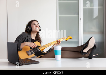 Geschäftsfrau Gitarre spielen am Schreibtisch Stockfoto