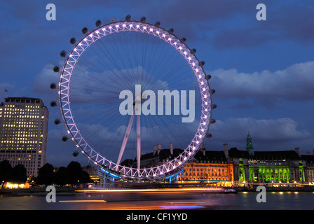 Blick auf das London Eye in der Abenddämmerung mit Booten entlang der Themse im Vordergrund. Stockfoto