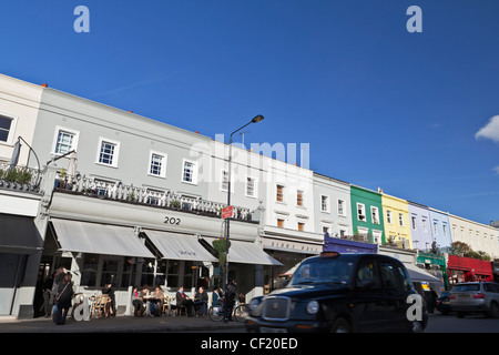 Ein schwarzes Londoner Taxi, vorbei an einer Reihe von Geschäften und Restaurants in Westbourne Grove. Stockfoto