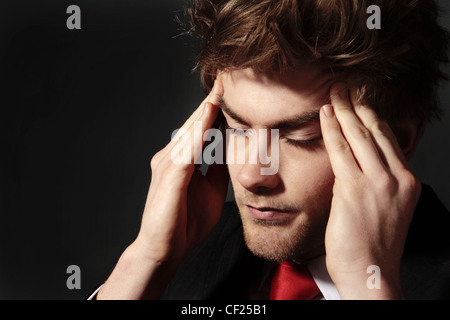 niedrige Schlüsselbild eines jungen Mannes, der Stress seine Schläfen reiben aussieht Stockfoto