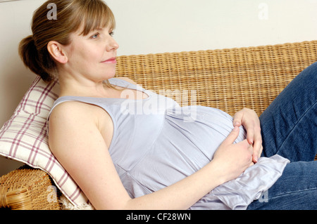 Trächtige Weibchen auf Wicker Sofa liegend mit Hände ruhen auf Stoß Stockfoto