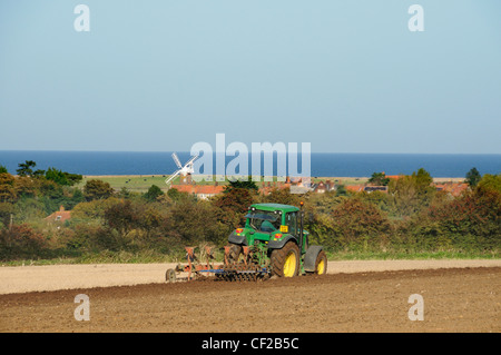 Traktor mit kombinierten Pflug und Scheibenegge auf küstennahen Ackerland mit Cley Windmühle in der Ferne. Stockfoto