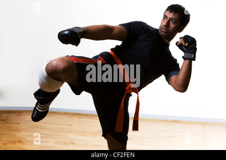 Ein Mann in einem Studio in einer üben eine Martial-Arts-Bewegung tragen Boxhandschuhe und einem Gürtel Stockfoto