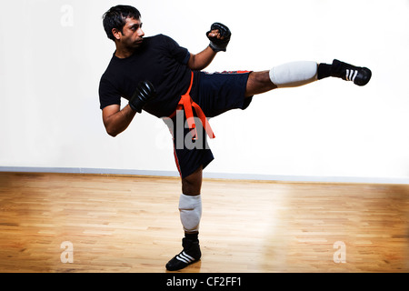 Ein Mann in einem Studio in einer üben eine Martial-Arts-Bewegung tragen Boxhandschuhe und einem Gürtel Stockfoto