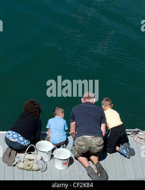 Eine Familie, kniend auf eine Anlegesteg Fischerei Krebse in Falmouth. Stockfoto