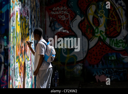 Ein Teenager schreiben an einer Wand bedeckt in Graffiti. Stockfoto