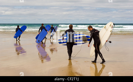 Eine Gruppe von Surfern mit ihren Surfbrettern, die ihren Weg über Fistral Strand heraus zum Meer. Stockfoto