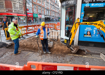 Auftragnehmer einen Graben in der Straße und Gehweg mit einem mechanischen Bagger, Leicester, England. Stockfoto