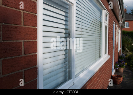 Weiß gerahmte Fenster mit weißen blind in Ziegelmauer an Vorderseite des Hauses in spitzen Winkel Stockfoto