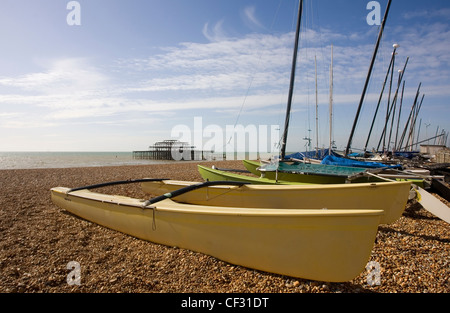 Kleine Katamarane auf den Kiesstrand in Brighton mit den Resten der West Pier im Hintergrund. Stockfoto