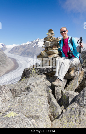 Sporttreibende und outdoor-Abenteuer: Frau auf Berggipfel mit Rucksack und Stöcken über Aletschgletscher der Schweiz Stockfoto