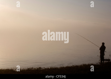 Die Silhouette der ein einsamer Angler Angeln im Bassenthwaite Lake im Lake District. Stockfoto