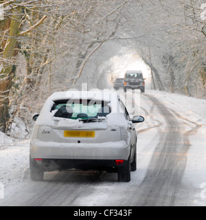 Rückansicht Ford Focus fährt auf schneebedeckten, von Bäumen gesäumten Landstraßen vor und nähert sich dem entgegenkommenden Verkehr im Winter Essex England Stockfoto