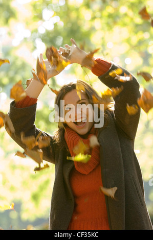 Frauen tragen orange Rollkragen Pullover, verlässt braunen Mantel zu werfen, in Luft, Hände über Kopf Stockfoto