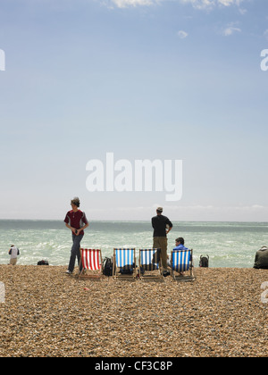Liegestühle und Menschen auf Brighton Strand an einem sonnigen Tag mit blauem Himmel. Stockfoto
