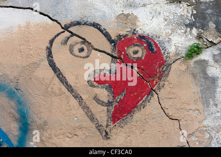 ein Riss durch einen gemalten Herzen ähnelt ein Gesicht an der Wand Stockfoto