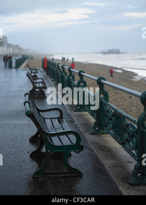 Eine Reihe von Bänken am Brighton Seafront an einem verregneten Tag mit dem Pier in der Ferne. Stockfoto