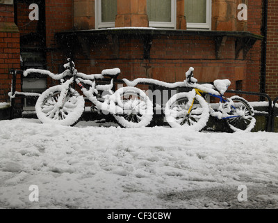 Zwei Fahrräder mit Geländer in Hove gelehnt Schnee bedeckt. Stockfoto