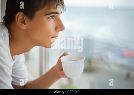 junge Teenager mit Tasse in der hand Blick aus Fenster morgens, Fokus auf Tasse Stockfoto