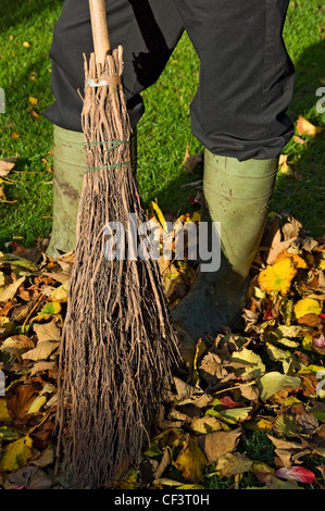 Nahaufnahme eines Mannes fegt Blätter auf einer Wiese im Herbst. Stockfoto